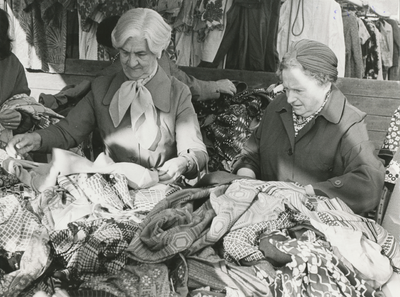 862624 Afbeelding van twee dames bij een uitstalling van tweedehands kleding en stoffen op de zaterdagse rommelmarkt in ...